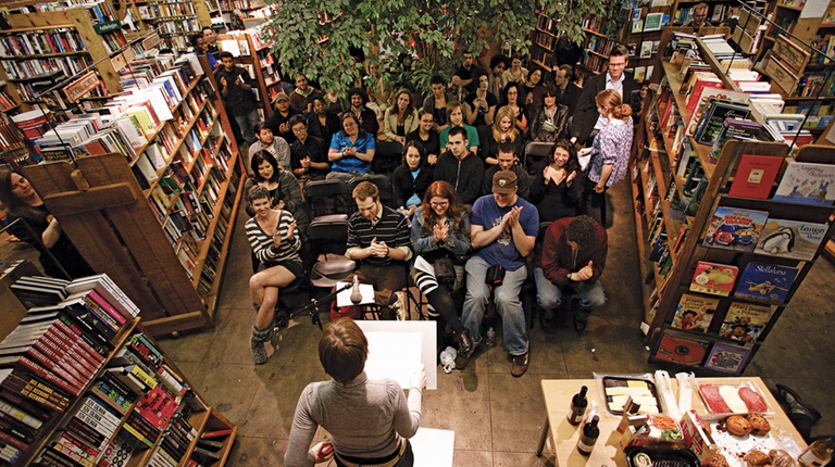 An audience watches a person speak at a podium. 