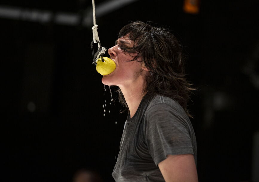 Faye Driscoll grabs a yellow ball with her mouth.