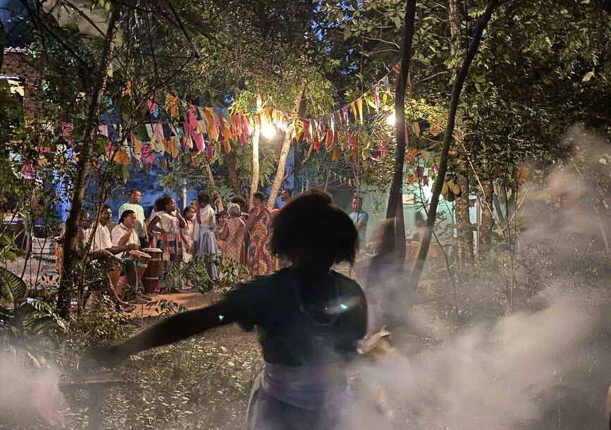 A woman in shadow performing in front of a screen depicting people in a forest from Christiane Jatahy: Depois Do Silêncio (After the Silence).