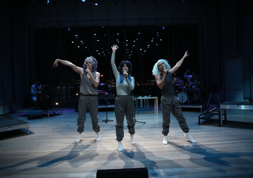 Three people stand with microphones on stage.