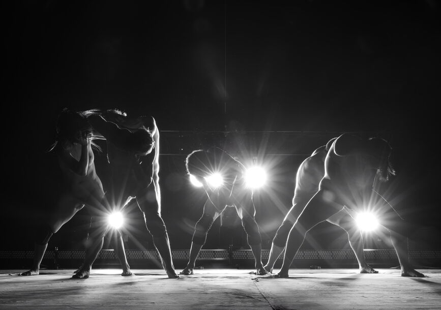 Nude people dance in front of lights.