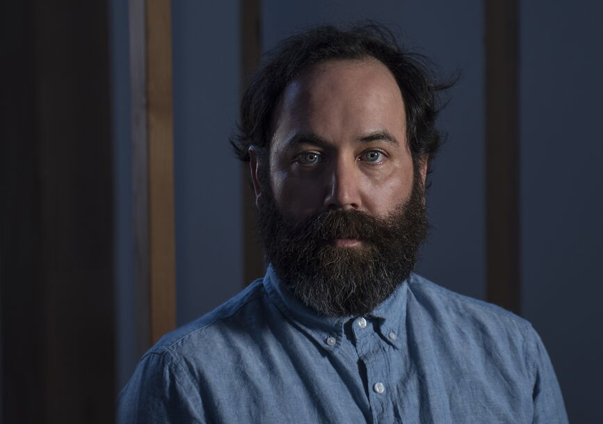 A man in a blue shirt sits in front of a blue wall.