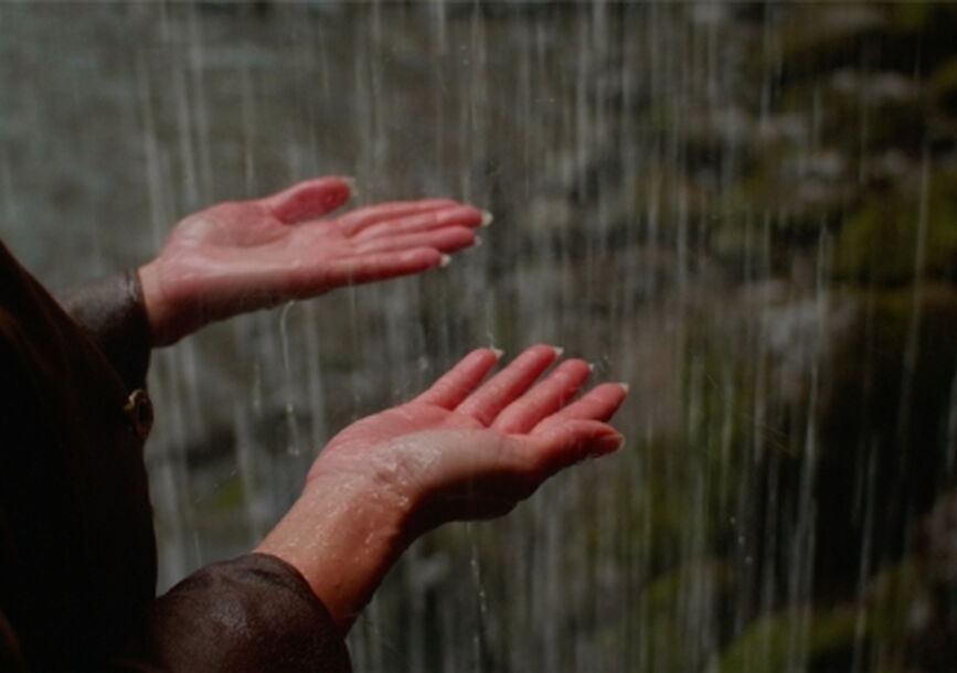 person with hands out feeling rain pouring 