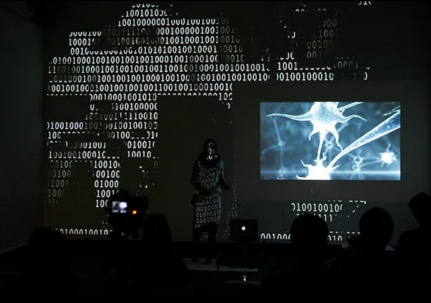 A person stands in front of projected images.