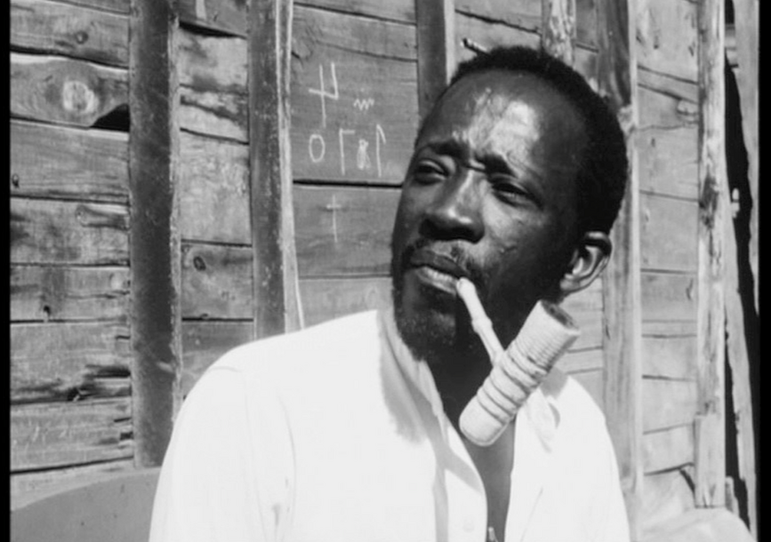 A person in front of a wooden wall with a pipe in their mouth.