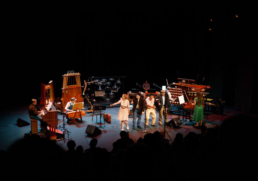 Musicians stand on stage with instruments.