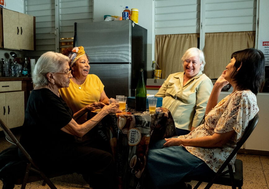 4 women sitting around a kitchen dining table laughing