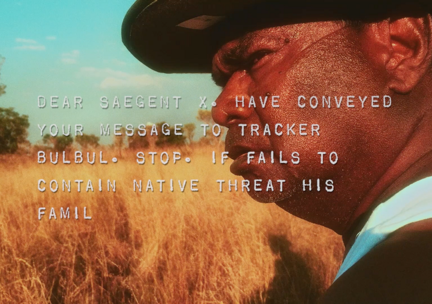 man with a hat standing in a field of yellow grass, staring hard in the left direction