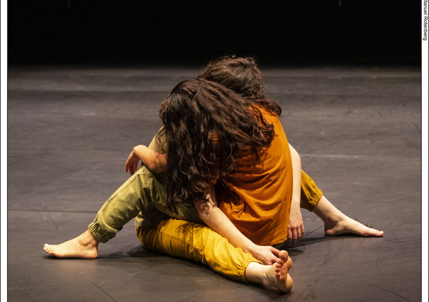 2 performers holding each other on stage in a performance. they are both on the ground. 