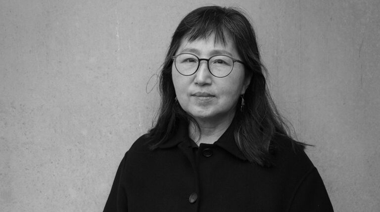 Don Mee stands against a wall. 