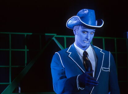 A blue person with a cowboy hat looks at the camera.