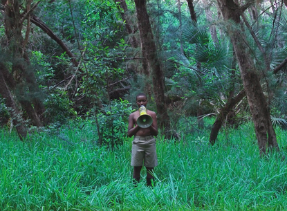 A person stands with a megaphone in the middle of a forest.