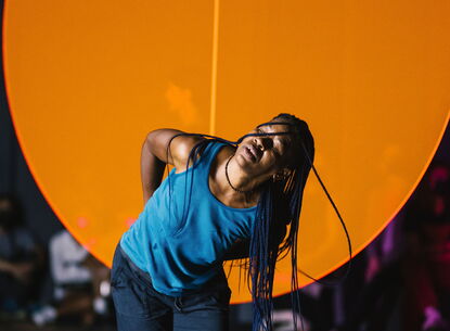 Okwui dances in front of a large orange circle.