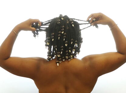 A person lifts their hands to hold their braids.