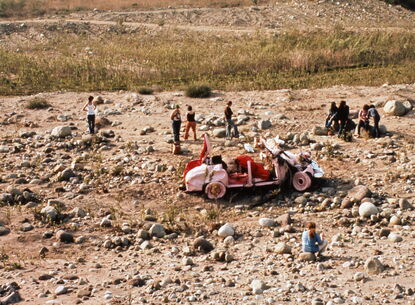 A pink car surrounded by people in a desert.