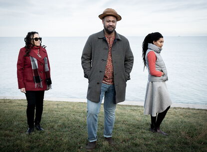 photo of 3 musicians standing in scenic background with grass and then the ocean
