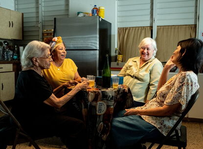 4 women sitting around a kitchen dining table laughing