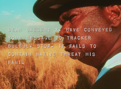 man with a hat standing in a field of yellow grass, staring hard in the left direction