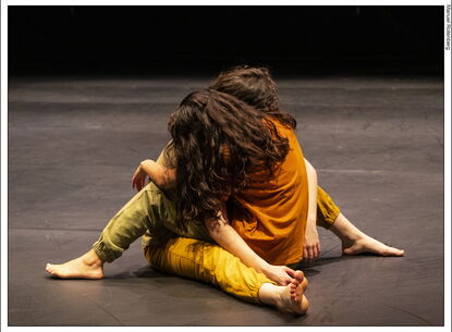 2 performers holding each other on stage in a performance. they are both on the ground. 